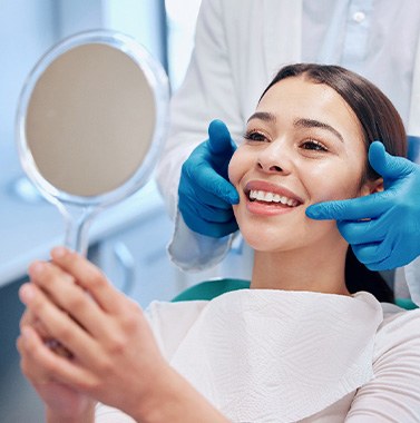 a smiling woman looking in a handheld mirror in a dental office