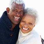 An older couple smiling and hugging after receiving their new restorations and more permanent smiles