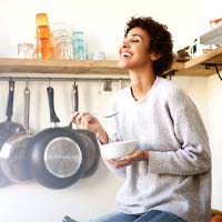 a person sitting on a counter in their kitchen and eating food out of a bowl