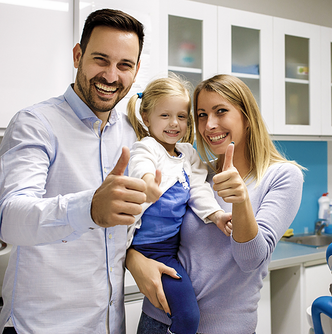 Mother, father, and their toddler all giving thumbs up in the dental office