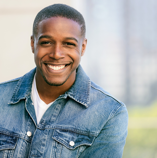 Man in a denim jacket smiling outdoors