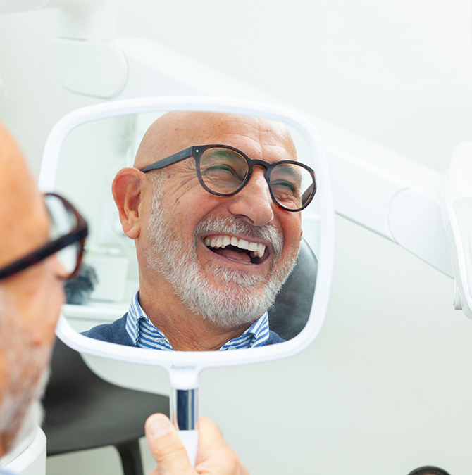 Dental patient admiring his new smile in a mirror