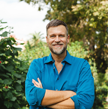 Man in a dark blue button-down shirt smiling among trees