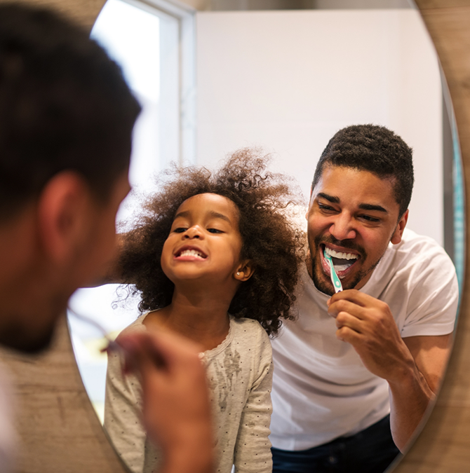 Man and his toddler daughter brushing their teeth together
