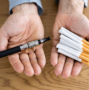 Hands holding cigarettes and a vape