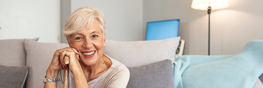 Senior woman with dentures in Bellingham sitting on a couch and leaning on her cane