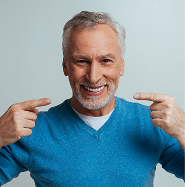 Senior man in a blue sweater pointing to his smile