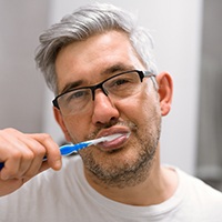 Senior man with glasses brushing his teeth