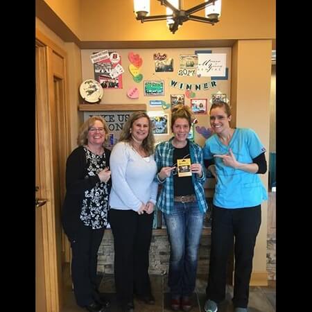 Woman smiling and holding giftcard with dental team