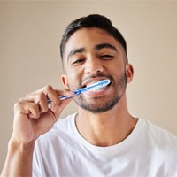 : Man in white shirt smiling and brushing his teeth 