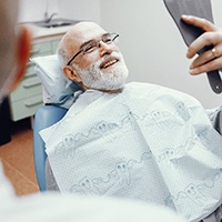 senior man admiring his smile after getting implant dentures 