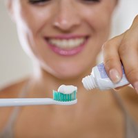 woman putting toothpaste onto an electric toothbrush 