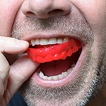 man putting a red mouthguard in his mouth 