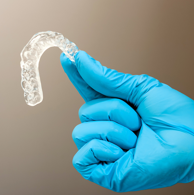 Gloved hand holding a clear nightguard