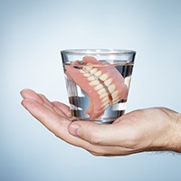 Hand holding glass of water with full denture