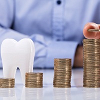 Person stacking coins next to a tooth