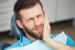 Grimacing man holding cheek in dental chair