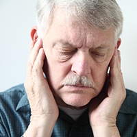 Man frowning with hands over ears