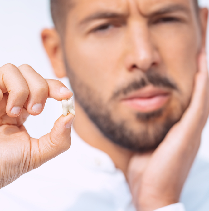 Man holding his extracted tooth and rubbing his cheek in pain
