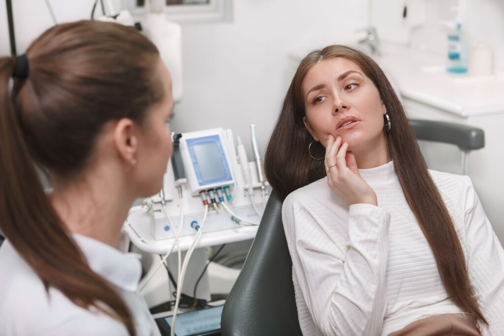 Young woman with long hair in dental chair touching chin in pain