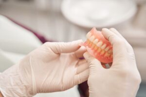 Gloved hands holding a set of full dentures. 