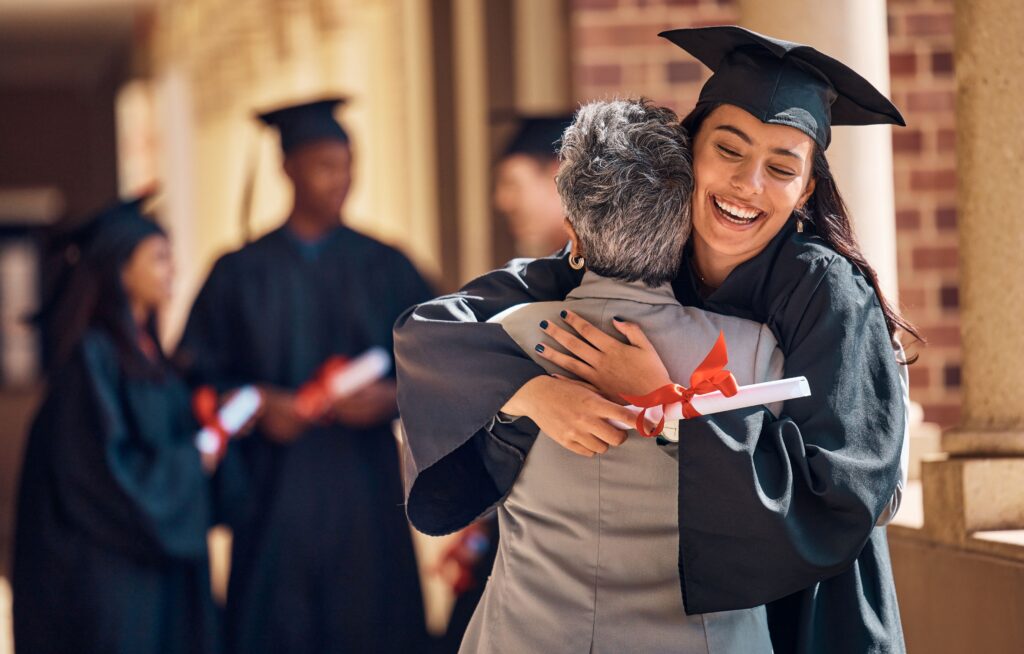 Teen in graduation cap and robe hugging family member