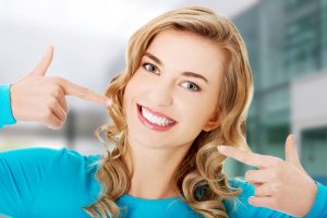 Woman with blond hair smiling and pointing to her teeth