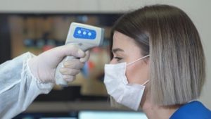 Woman wearing a mask and getting her temperature taken with an electric thermometer