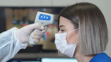 Woman wearing a mask and getting her temperature taken with an electric thermometer.